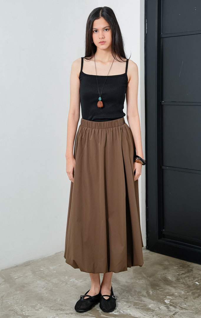 Rok panjang wanita mengalir (flowy long skirt) warna cokelat (brown) Irwin Skirt dengan siluet balon halus (subtle balloon silhouette), pinggang karet elastis yang nyaman (comfortable stretch waistband), dan saku samping (side pockets).