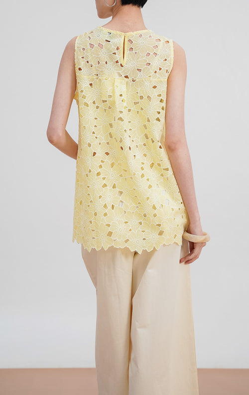 Tampilan belakang model mengenakan Iverna Top warna yellow, atasan tanpa lengan dengan detail bordir bunga eyelet di seluruh bagian dan bukaan kancing di leher belakang.