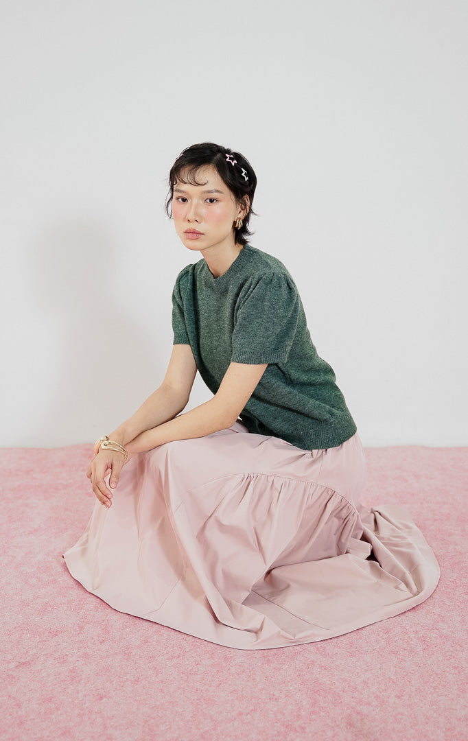 Atasan rajut wanita Jaeyun Top dari This Is April warna Dark Green dengan kerah bulat dan lengan pendek model puff (balon), dipadukan dengan rok panjang warna pink.