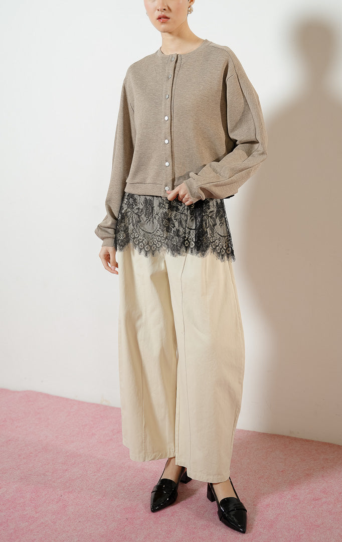 Model wanita mengenakan Oulia Jacket warna taupe, jaket cardigan rajut jersey wanita berwarna cokelat dengan kancing jepret metalik dan detail kelim renda brokat hitam transparan yang anggun.