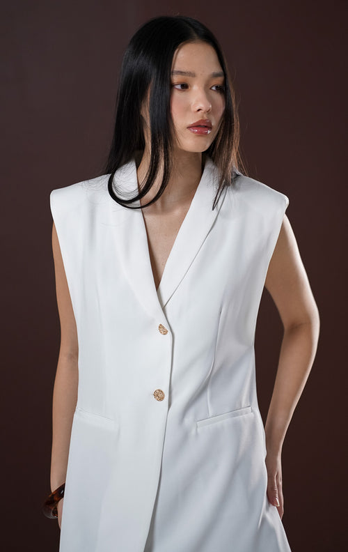 Gaun blazer pendek wanita (blazer dress) Jeane warna putih bersih tanpa lengan menampilkan kerah lapel formal, satu kancing depan, saku dekoratif, dan potongan bahu yang tegas.