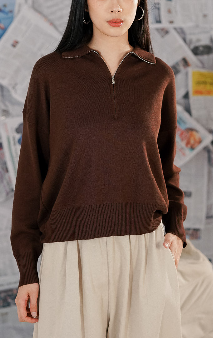 Wanita mengenakan Jett Sweater warna coklat polos (brown), sweater rajut lengan panjang dengan kerah resleting (half zip) dan potongan relaxed fit yang minimalis.1