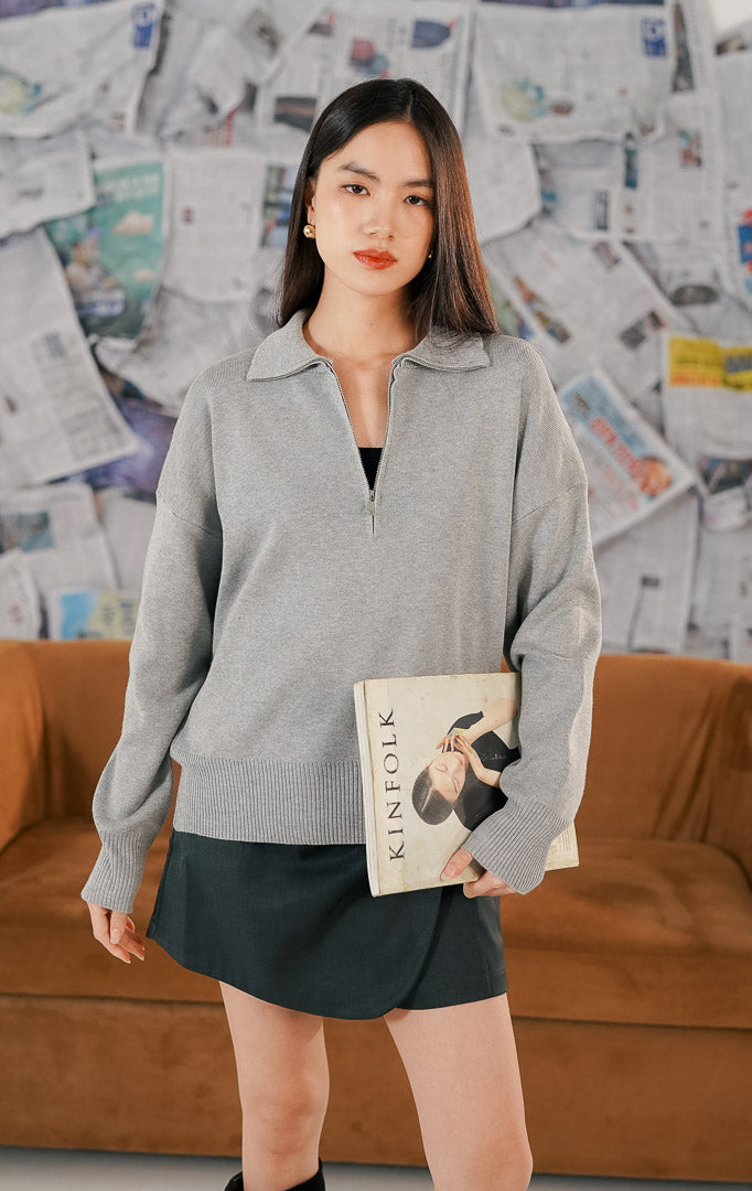 Jett Sweater warna abu-abu (grey), atasan rajut lengan panjang polos dengan kerah resleting (half zip) yang modern, dipadukan dengan rok mini.
