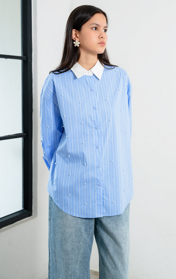Kemeja wanita lengan panjang motif garis-garis biru (blue striped) Jeyra Top dengan aksen hiasan mutiara (pearl embellishments), kerah dan manset kontras warna putih (contrasting collar and cuffs), serta kelim melengkung (curved hem).