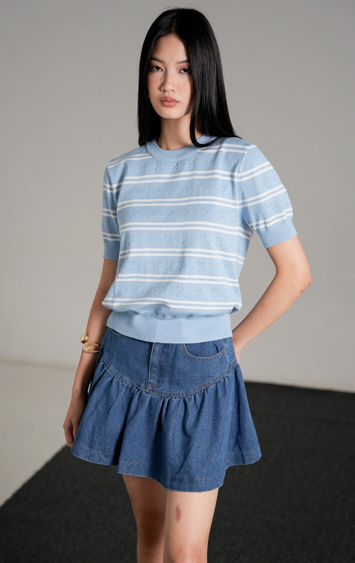 Jourdan Top, atasan rajut lengan pendek motif garis biru putih, dipadukan dengan rok mini denim biru dan sepatu hak hitam.