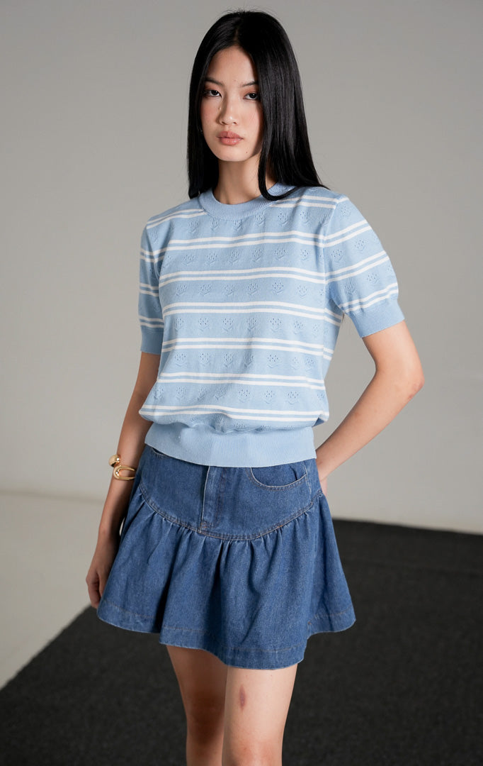 Jourdan Top, atasan rajut lengan pendek motif garis biru putih, dipadukan dengan rok mini denim biru dan sepatu hak hitam.