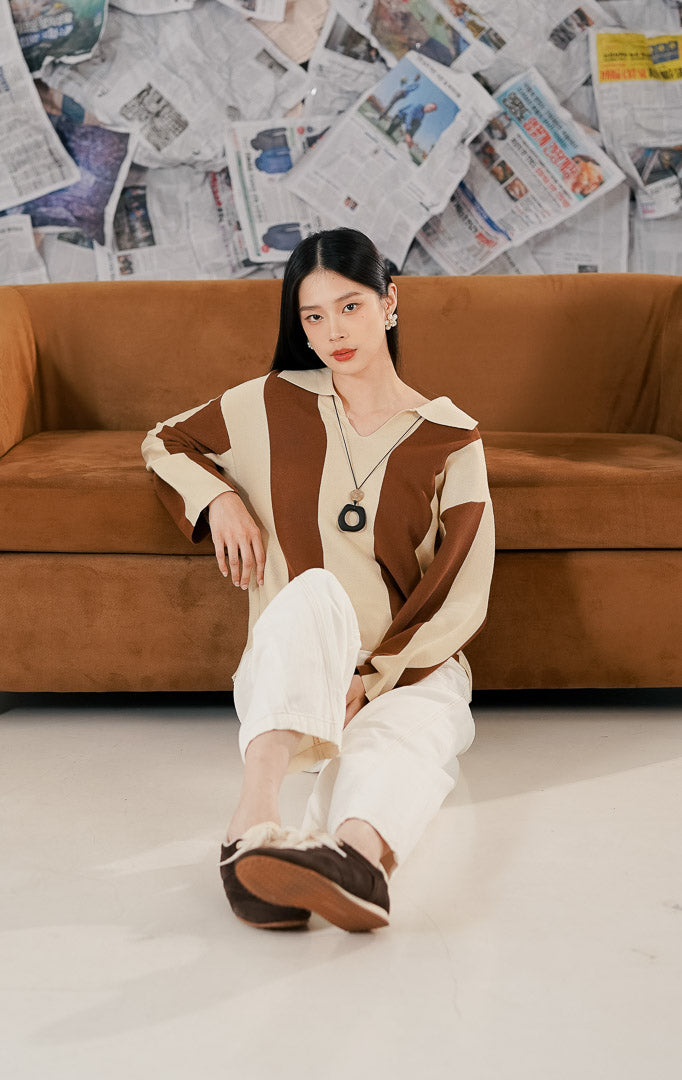 Model wanita memakai Justin Sweater Brown, sebuah atasan sweater rajut lengan panjang dengan motif garis-garis vertikal lebar kombinasi warna cokelat bata (terracotta) dan krem, serta kerah model V-neck.