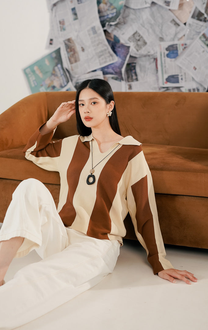 Model wanita memakai Justin Sweater Brown, sebuah atasan sweater rajut lengan panjang dengan motif garis-garis vertikal lebar kombinasi warna cokelat bata (terracotta) dan krem, serta kerah model V-neck.1