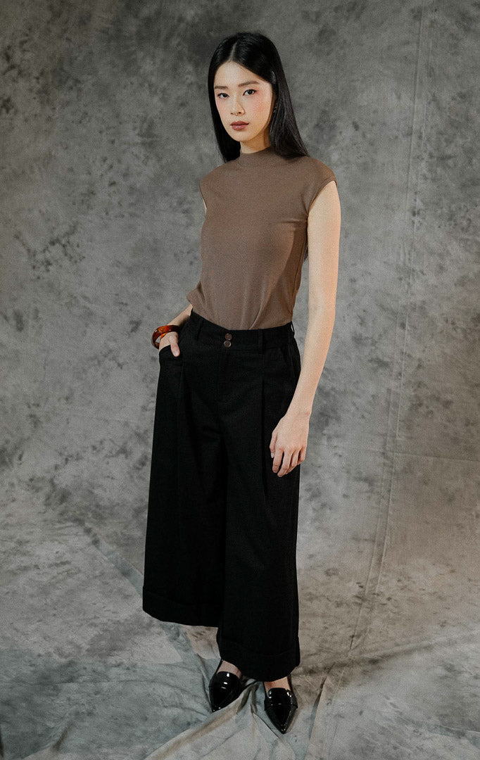 Celana panjang kulot wanita Kahi warna hitam dengan cutting wide leg, detail double kancing depan, saku samping, dan aksen lipatan besar di ujung bawah.