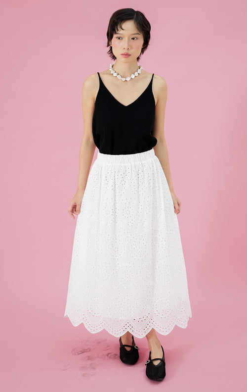 Rok putih wanita Kassidy Skirt dari This Is April dengan detail bordir eyelet seluruh bagian dan potongan pinggir bawah bergelombang (scalloped), dipadukan dengan tank top hitam.