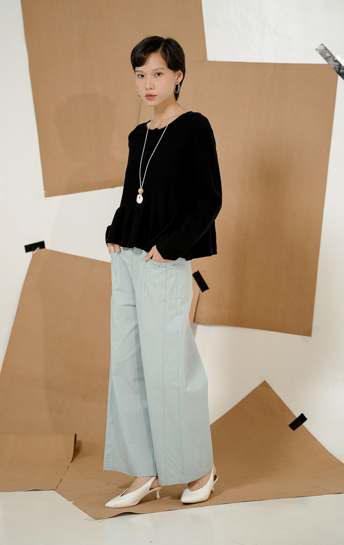 Model berdiri mengenakan Keeley Button-up Peplum Knit Cardigan Black, produk luaran cardigan rajut wanita warna hitam dengan kancing depan dan potongan peplum bergelombang.