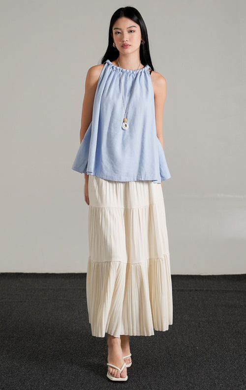 Keilani Top Light Blue, atasan tanpa lengan warna biru muda dengan detail kerah kepang (braided neckline), dipadukan dengan rok panjang lipit putih.