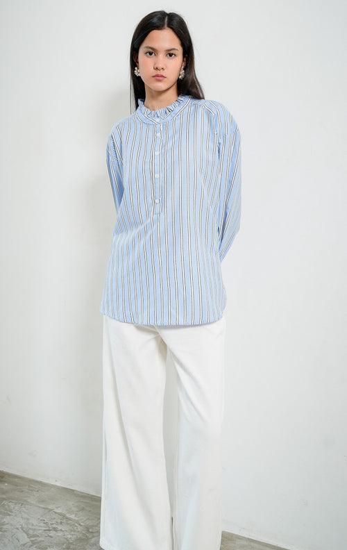 Blus wanita lengan panjang motif garis-garis biru (blue striped) Kellie Top berbahan kain tenun ringan (lightweight woven fabric) dengan kerah berdiri aksen kerut (ruffled stand neckline), bukaan setengah kancing depan (half-placket), dan kelim melengkung (curved hem).