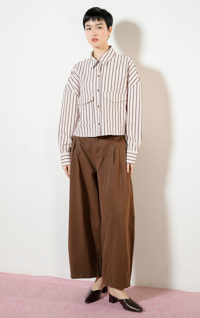 Model wanita mengenakan Georgette Classic Striped Collared Crop Shirt warna light pink, kemeja crop salur wanita lengan panjang berwarna merah muda dengan dua saku depan.