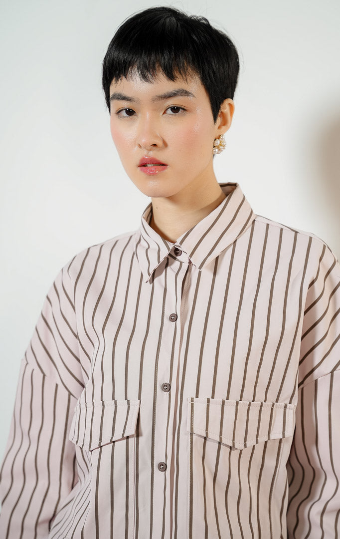Model wanita mengenakan Georgette Classic Striped Collared Crop Shirt warna light pink, kemeja crop salur wanita lengan panjang berwarna merah muda dengan dua saku depan.