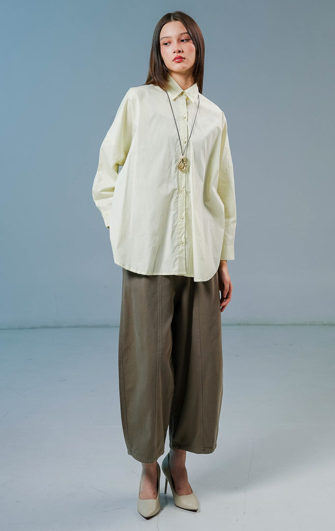 Model wanita mengenakan kemeja lengan panjang Dayle Top warna kuning muda berpotongan longgar (oversize) dengan detail kancing depan.
