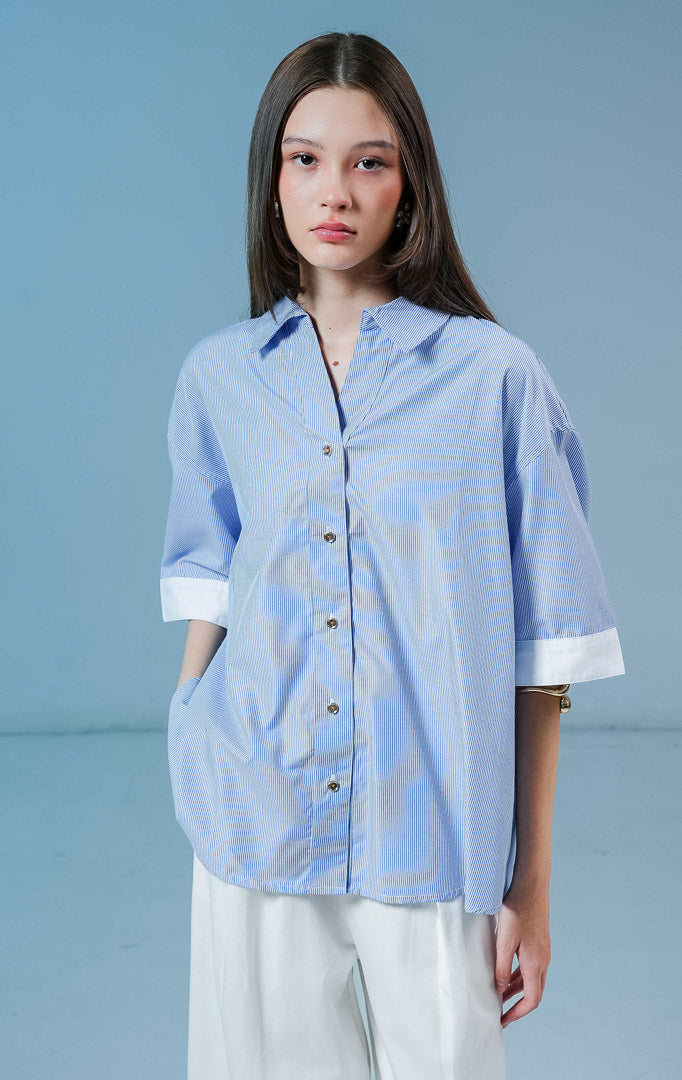 Model wanita mengenakan Naudre Stripe Contrast Hem Top warna blue, kemeja salur wanita motif garis biru-putih dengan detail ujung lengan putih kontras yang modern.