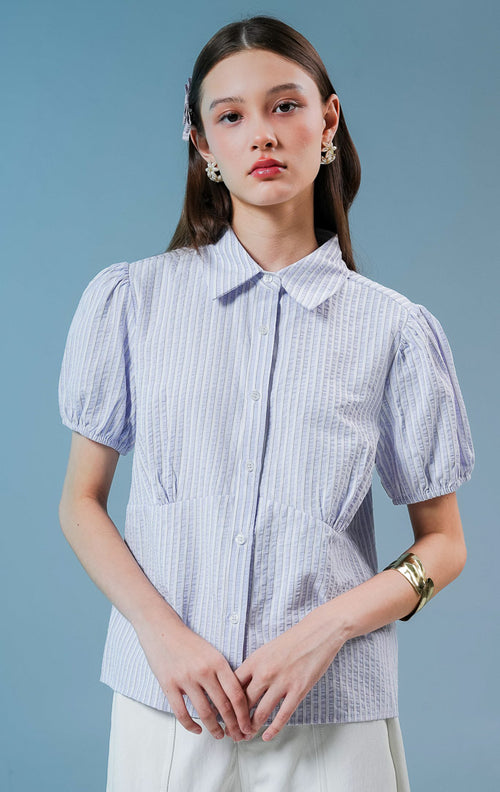 Model wanita mengenakan Theana Collared Puff Sleeve Top warna light purple, blouse kemeja salur wanita motif garis ungu-putih dengan lengan balon pendek dan detail siluet pinggang berstruktur