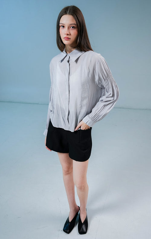 Model wanita mengenakan Milano Gathered Sleeve Collared Sheer Top warna light grey, kemeja lengan panjang transparan wanita dengan detail kerutan lengan yang elegan.