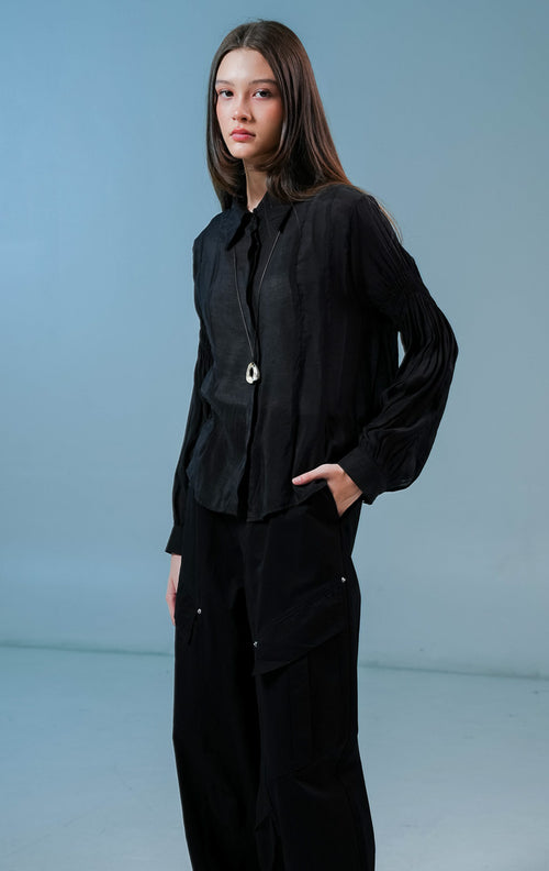 Model wanita mengenakan Milano Gathered Sleeve Collared Sheer Top warna hitam, kemeja lengan panjang transparan wanita dengan detail kerutan lengan yang elegan.