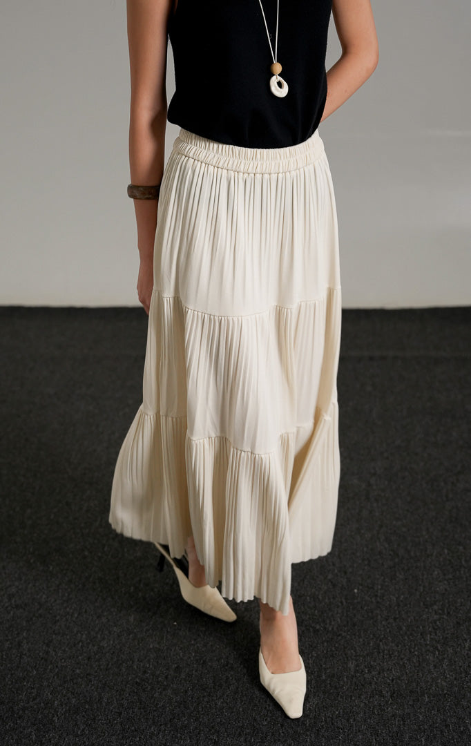 Kenny Skirt Ivory, rok panjang lipit bertingkat warna krem dengan pinggang karet, dipadukan dengan tank top hitam dan kalung.