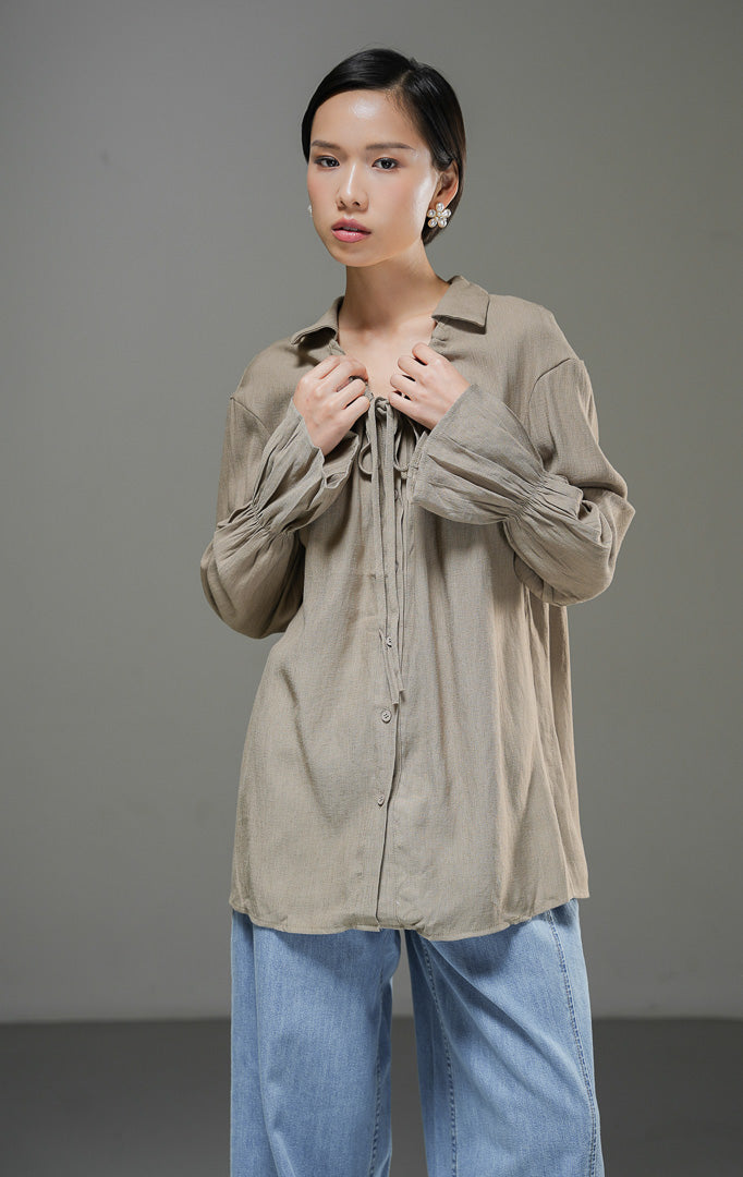 Blouse wanita Kensley Top warna brown cokelat lengan panjang dengan detail tali pita leher (tie neck), kerah kemeja, dan kancing depan.