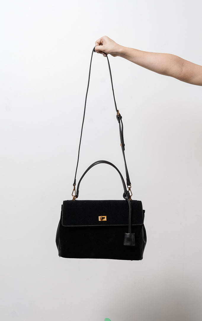 Tas wanita Lalitha warna hitam menampilkan kombinasi bahan kulit sintetis dan suede bertekstur lembut, penutup flap dengan kunci putar (twist lock) warna emas, lengkap dengan tali jinjing pendek (handbag) serta tali panjang (sling bag).