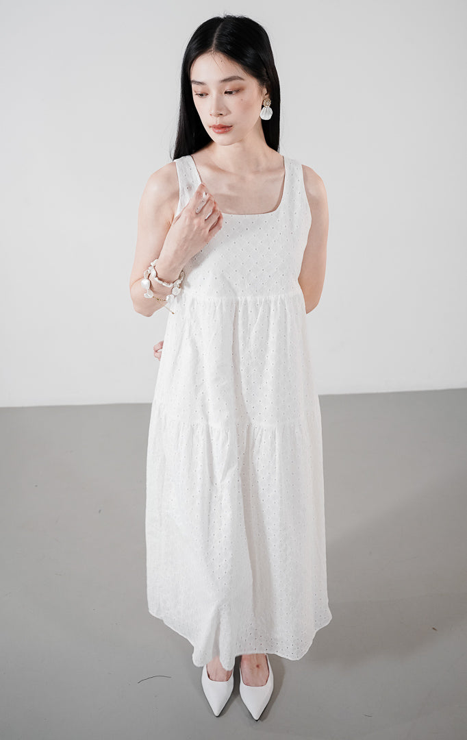 Model wanita mengenakan Layila Dress warna white, gaun mini tanpa lengan dengan detail bordir eyelet floral di seluruh kain dan siluet tiered yang feminin.