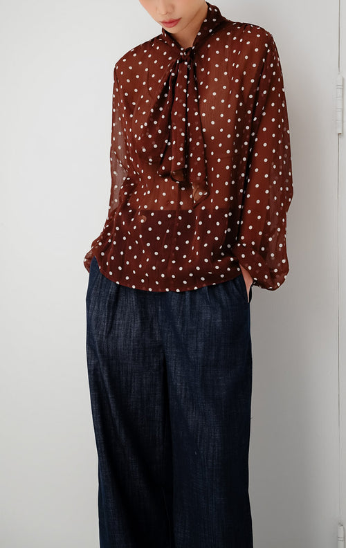 Atasan chiffon wanita transparan (sheer) warna cokelat tua (dark brown) Lillith Top motif polkadot dengan aksen ikatan leher (tie-neck) dan lengan panjang.