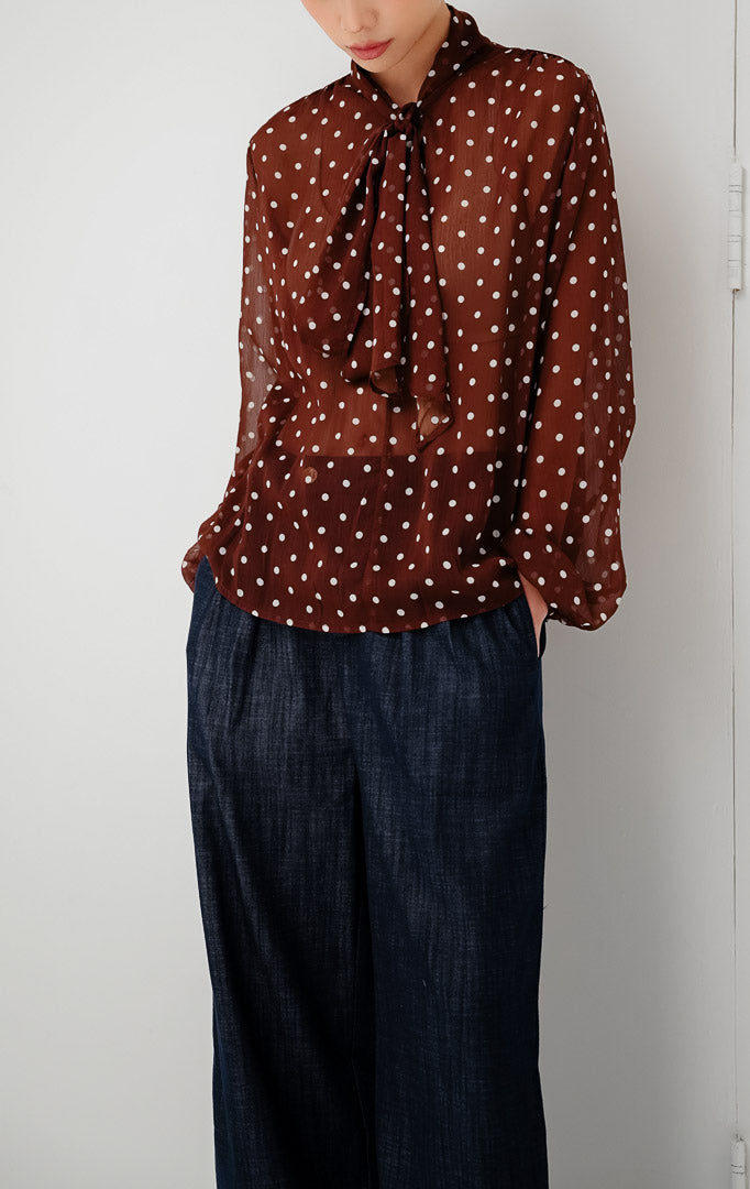 Atasan chiffon wanita transparan (sheer) warna cokelat tua (dark brown) Lillith Top motif polkadot dengan aksen ikatan leher (tie-neck) dan lengan panjang.
