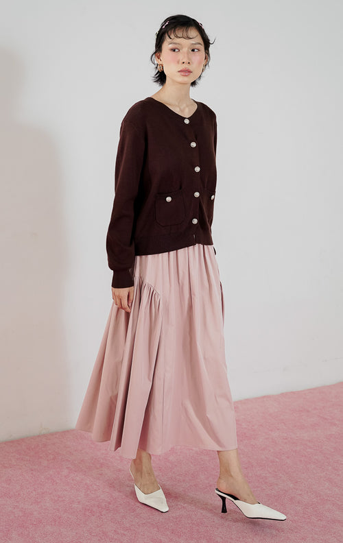 Kardigan rajut wanita Lily Cardigan warna cokelat tua (brown) dari This Is April dengan detail kancing emas dan kantong depan, dipadukan dengan rok midi pink.