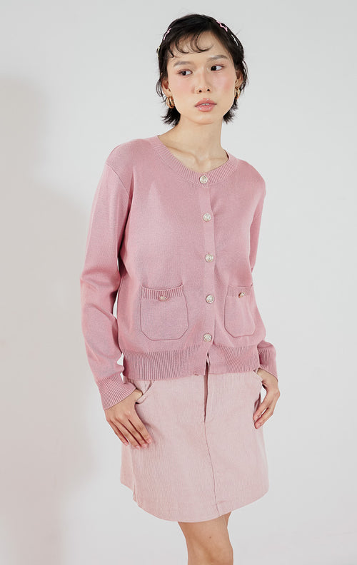 Atasan wanita Lily Cardigan warna pink dari This Is April dengan bahan rajut lembut, detail kancing emas (gold button), dan dua saku depan, dipadukan dengan rok mini pink senada.