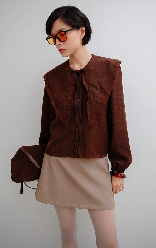 Atasan wanita warna cokelat Linara Top berbahan katun berstruktur dengan detail kerah scalloped Peter Pan untuk tampilan chic dan office look.