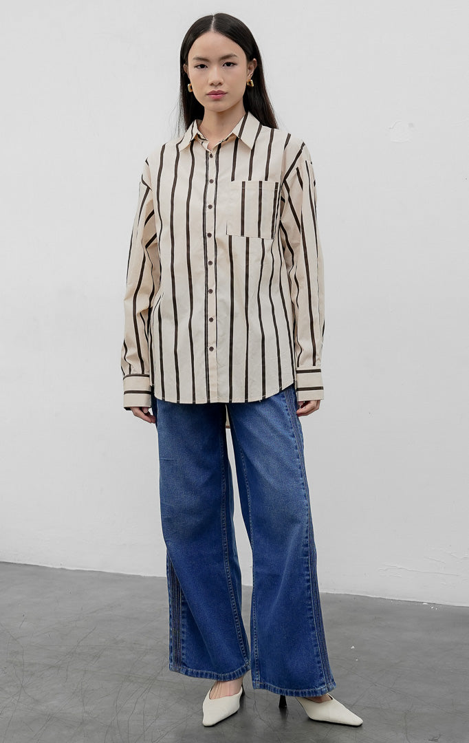Kemeja wanita oversized lengan panjang warna cokelat (brown) Linette Top bermotif garis vertikal (striped) berbahan campuran katun-poliester dengan saku depan fungsional.