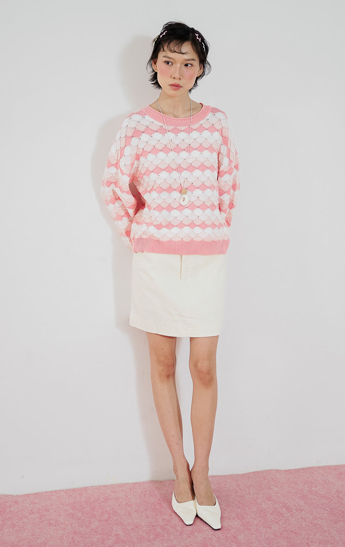 Atasan sweater rajut wanita Loryn warna pink putih dari This Is April dengan motif diamond (belah ketupat) dan kerah bulat, dipadukan dengan rok pendek putih.