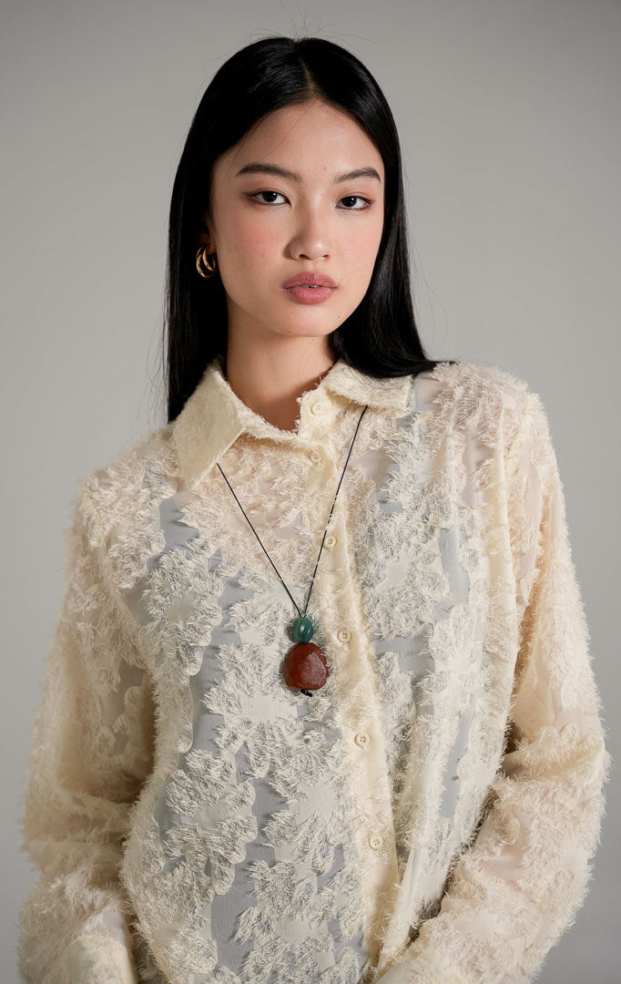 Loui Top Ivory, kemeja lengan panjang warna putih tulang semi-transparan dengan tekstur bulu halus, dipadukan dengan celana jeans biru.