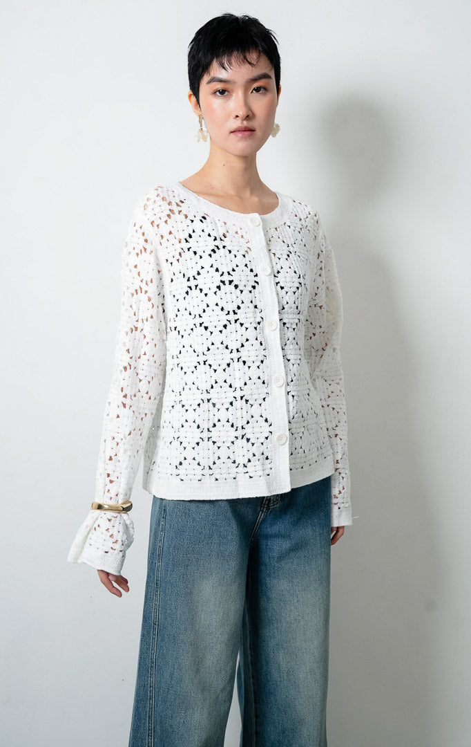 Kardigan rajut wanita lengan panjang warna putih (white) Lucia Cardigan berbahan rajut renda transparan (crochet open-knit) dengan kerah bulat (round neckline) dan bukaan kancing depan warna senada.