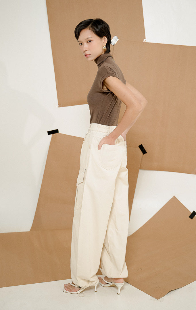 Model berpose dari samping mengenakan Lunaria Utility Bush Pants Ivory, produk celana panjang cargo wanita warna putih gading dengan detail saku utilitas samping