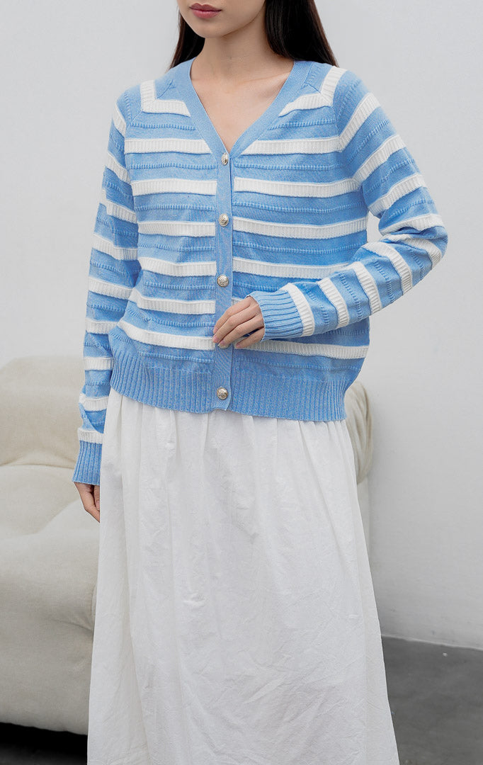 Kardigan rajut wanita lengan panjang warna biru muda (light blue) Matera Cardigan bermotif garis horizontal putih (striped) dengan kerah V (V-neck) dan kancing emas.