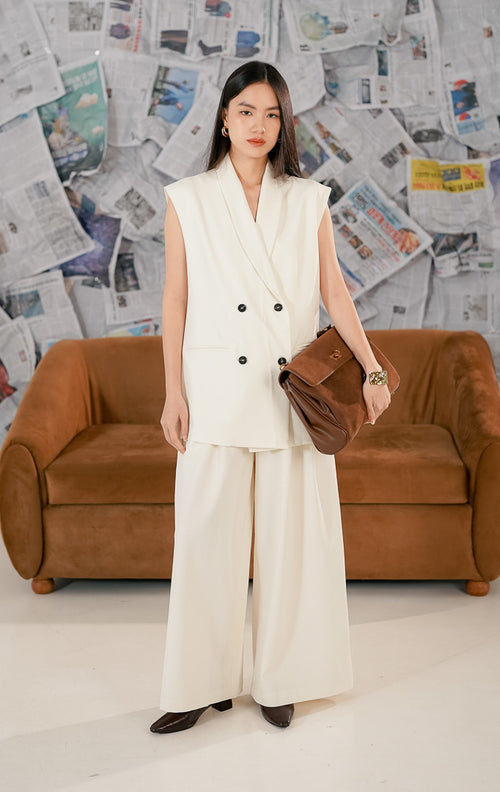 Model wanita mengenakan Mayara Vest warna putih, blazer tanpa lengan (sleeveless) model double breasted dengan kancing hitam dan kerah lapel, bergaya formal elegan.