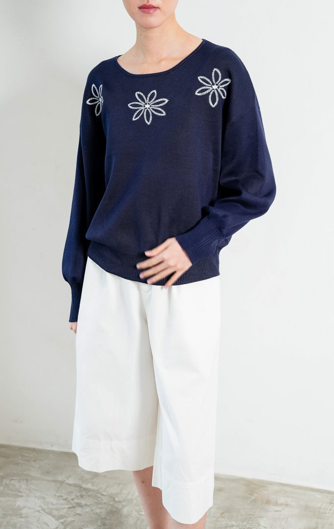 Sweter rajut wanita lengan panjang warna biru navy (navy blue) Mayra Sweater berbahan rajut lembut (soft knit) dengan kerah bulat (round neckline) dan aksen bordir bunga putih di bagian dada (white floral embroidery).