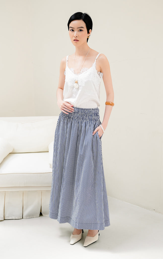 Rok panjang maxi wanita Mille Skirt warna navy bermotif stripe (garis-garis) berbahan katun dengan detail multi-row smocked waist yang elegan.
