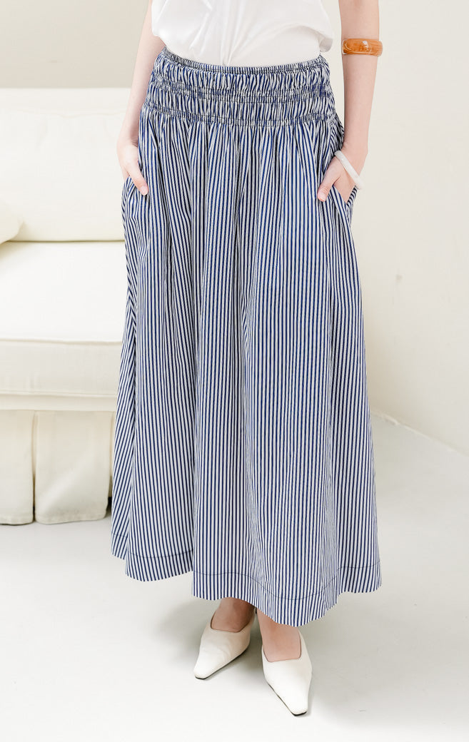 Rok panjang maxi wanita Mille Skirt warna navy bermotif stripe (garis-garis) berbahan katun dengan detail multi-row smocked waist yang elegan.
