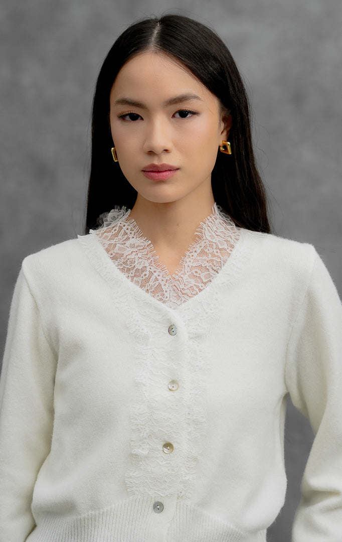 Sweter rajut wanita lengan panjang warna putih (white) Mirabel Sweater dengan kerah V (V-neck), aksen rendetan renda halus (lace trim), dan kancing depan.