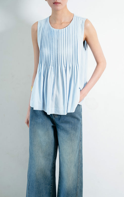 Atasan wanita tanpa lengan warna biru muda (light blue sleeveless top) Miuza Top berbahan kain tenun ringan dengan detail panel plisket vertikal di bagian depan (vertical pleated panels), kerah bulat (round neckline), serta bagian bawah berkerut yang lembut (softly gathered lower section).