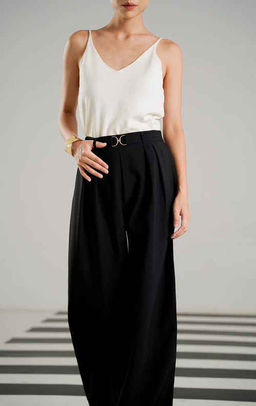 Celana panjang bahan wanita Monroe Pants Black dengan detail emblem logam emas di pinggang, aksen lipit depan (pleats), dan potongan kaki lurus.