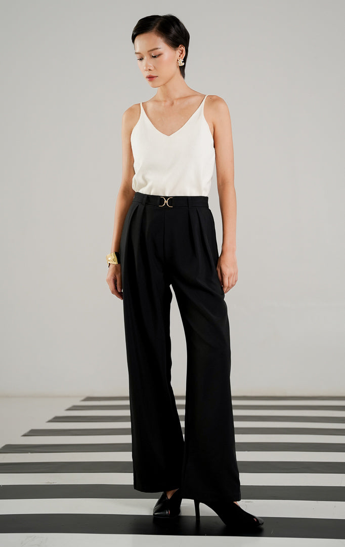Celana panjang bahan wanita Monroe Pants Black dengan detail emblem logam emas di pinggang, aksen lipit depan (pleats), dan potongan kaki lurus.