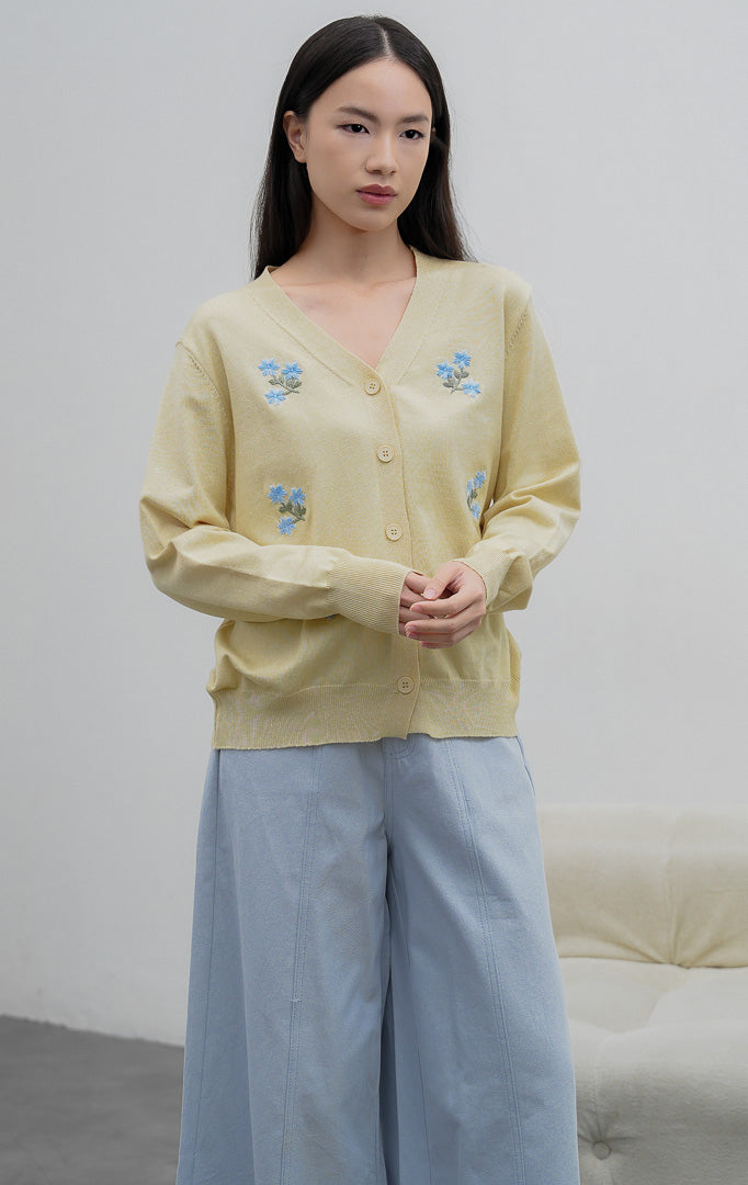 Kardigan rajut wanita lengan panjang warna kuning muda (butter yellow) Morlith Cardigan dengan kerah V (V-neck), bukaan kancing depan, dan aksen bordir bunga biru (floral embroidery).
