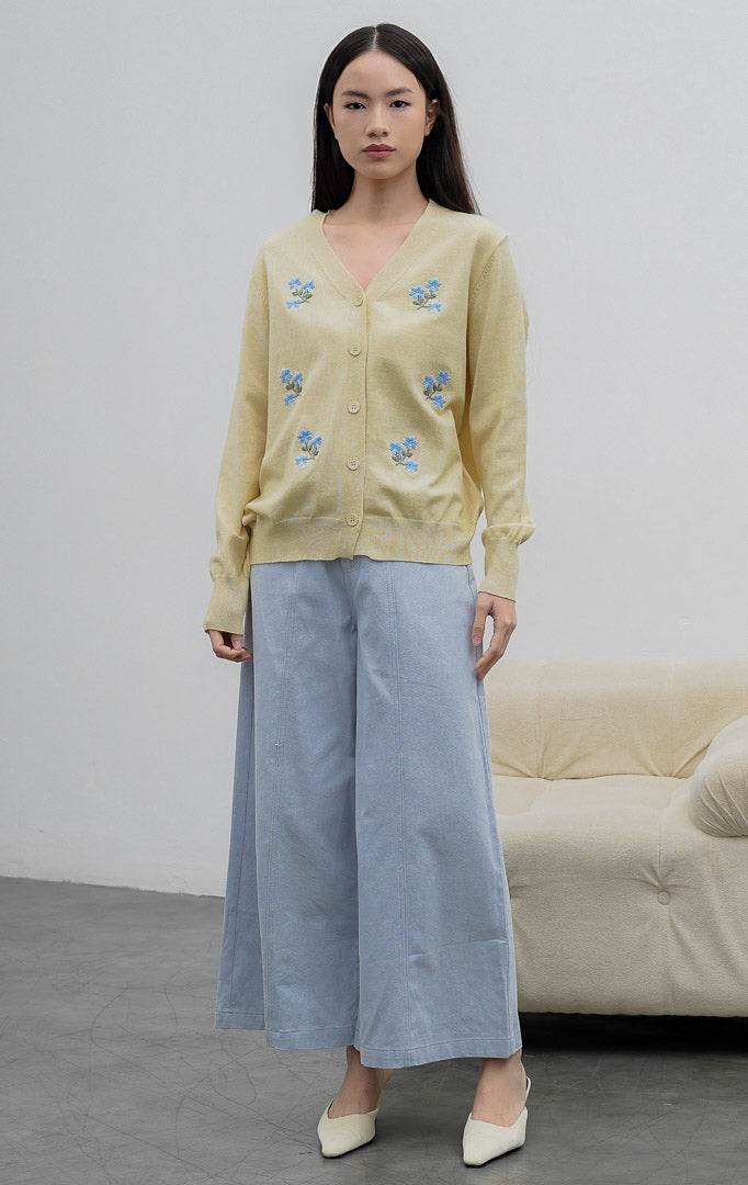 Kardigan rajut wanita lengan panjang warna kuning muda (butter yellow) Morlith Cardigan dengan kerah V (V-neck), bukaan kancing depan, dan aksen bordir bunga biru (floral embroidery).