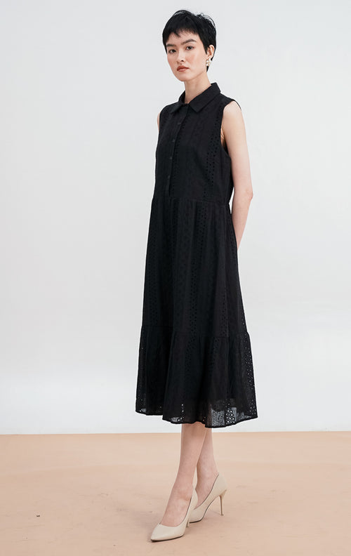 Model mengenakan Nalani Dress warna black, gaun maxi tanpa lengan dengan kerah kemeja, detail bordir eyelet di seluruh bagian, dan potongan bertingkat (tiered).